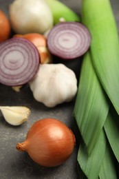 Fresh whole and cut onions, leeks, garlic on grey table, closeup