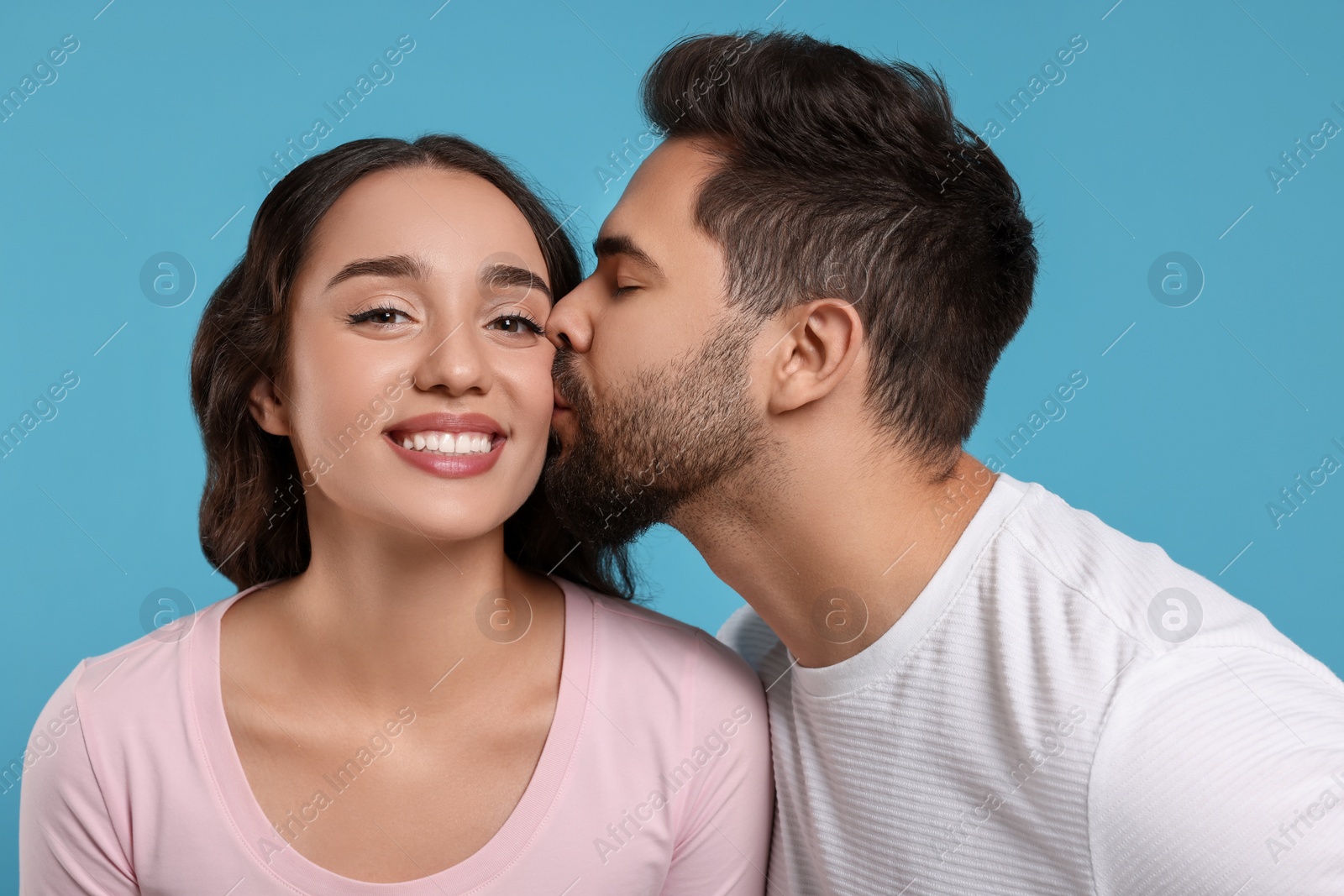 Photo of Man kissing his smiling girlfriend on light blue background