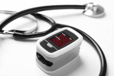 Modern fingertip pulse oximeter and stethoscope on white background, closeup