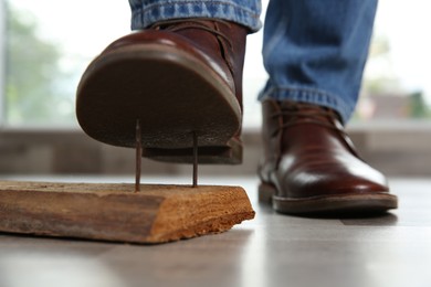 Photo of Careless man stepping on nails in wooden plank, closeup