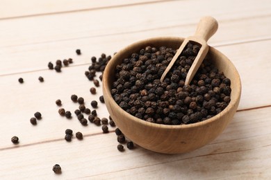 Photo of Aromatic spice. Black peppercorns and scoop in bowl on wooden table