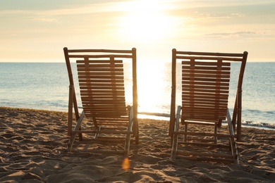 Wooden deck chairs on sandy beach at sunset. Summer vacation