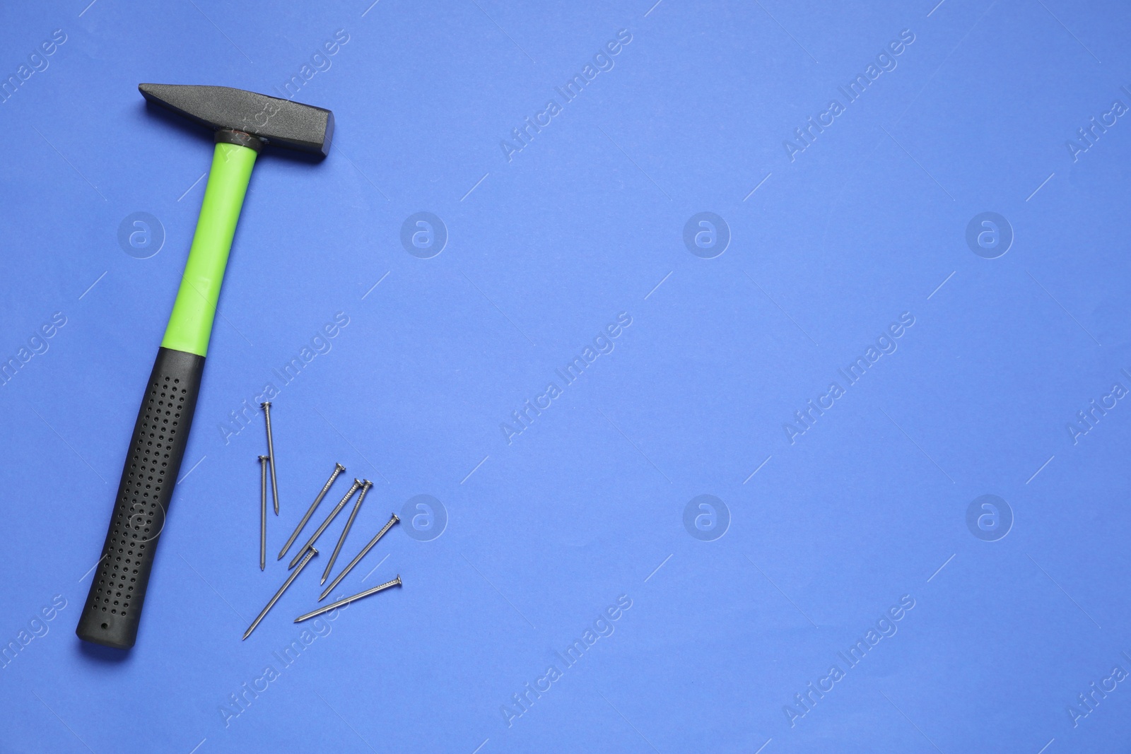 Photo of Hammer and metal nails on blue background, top view. Space for text