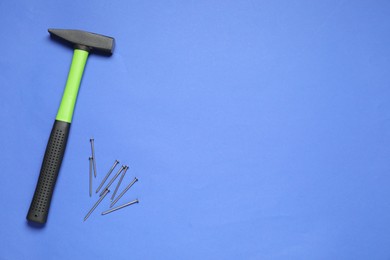 Hammer and metal nails on blue background, top view. Space for text