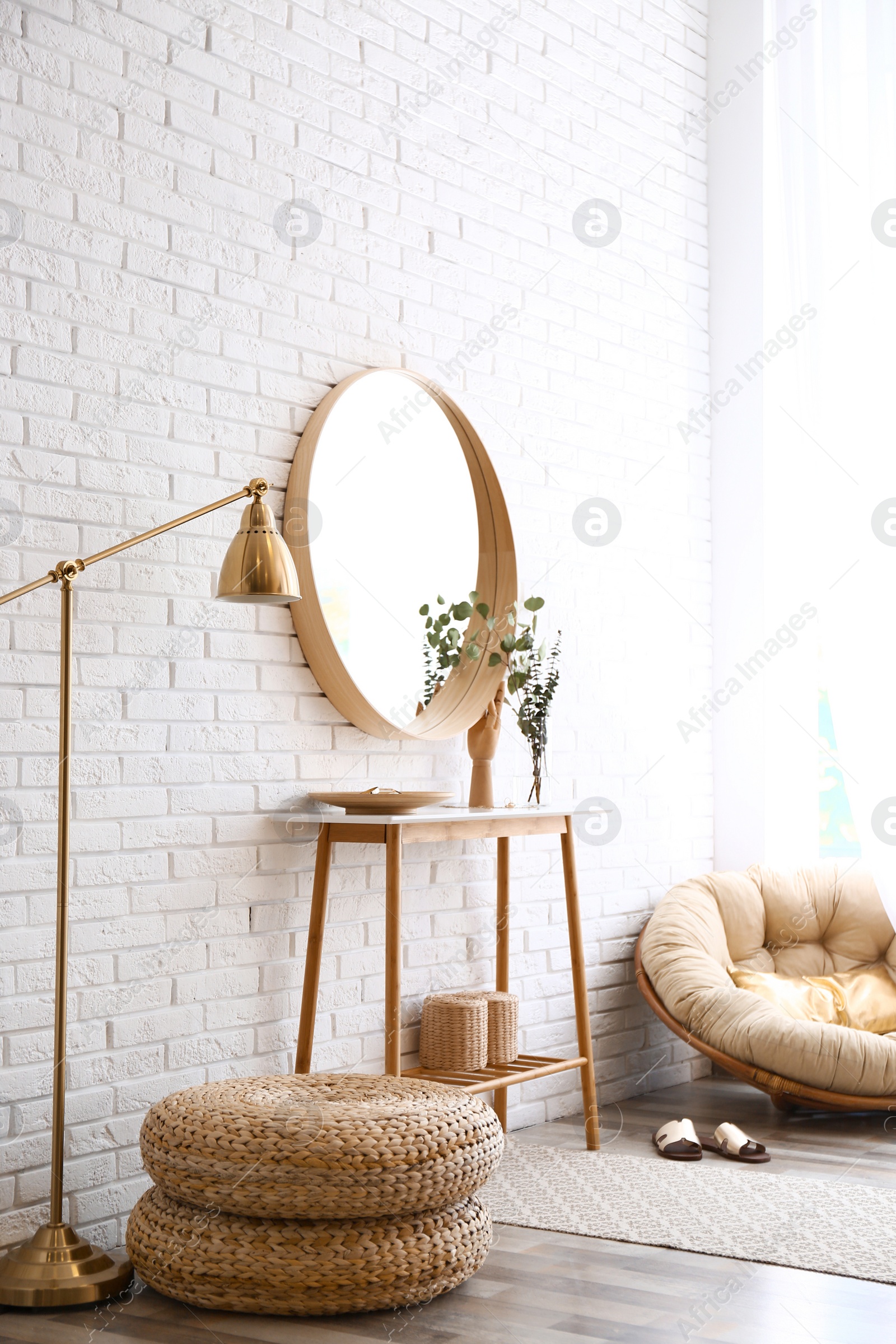 Photo of Hallway interior with big round mirror, table and decor near brick wall