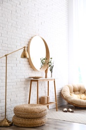 Hallway interior with big round mirror, table and decor near brick wall