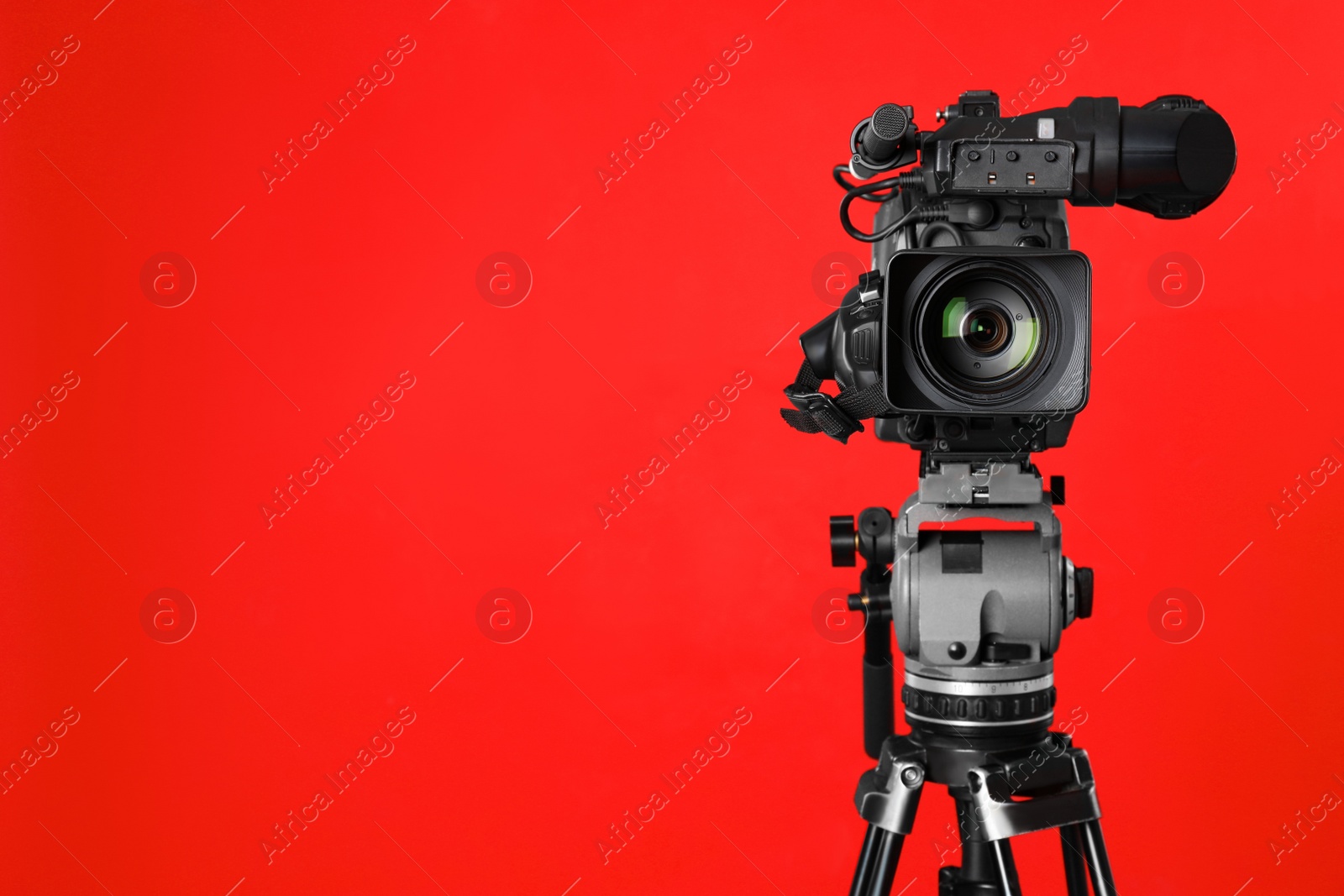 Photo of Modern professional video camera on red background. Space for text