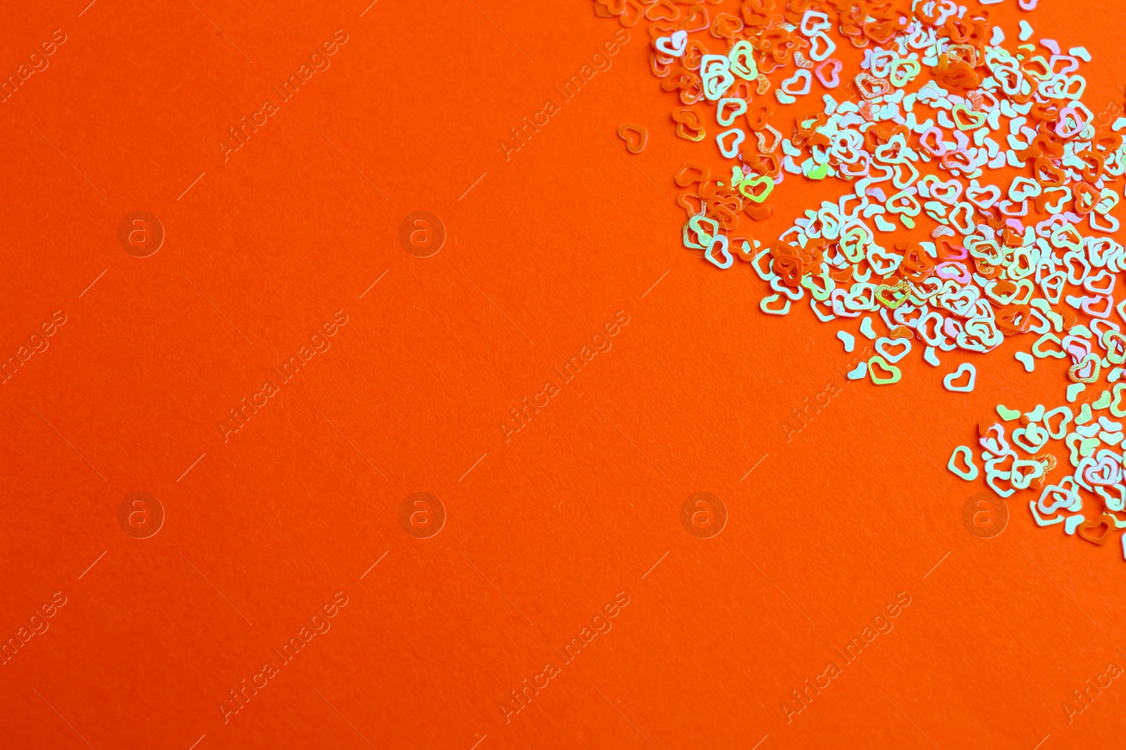 Photo of Shiny bright heart shaped glitter on coral background. Space for text