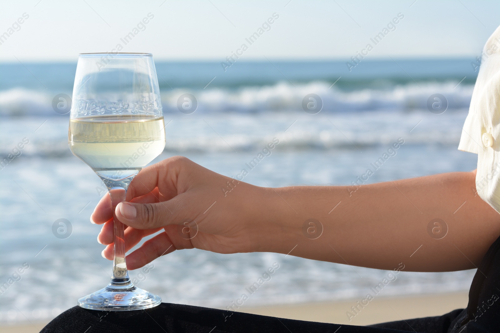 Photo of Woman with glass of tasty wine near sea, closeup