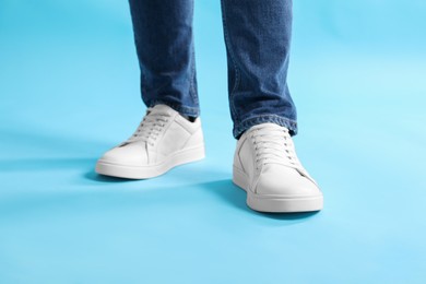 Man wearing stylish white sneakers on light blue background, closeup