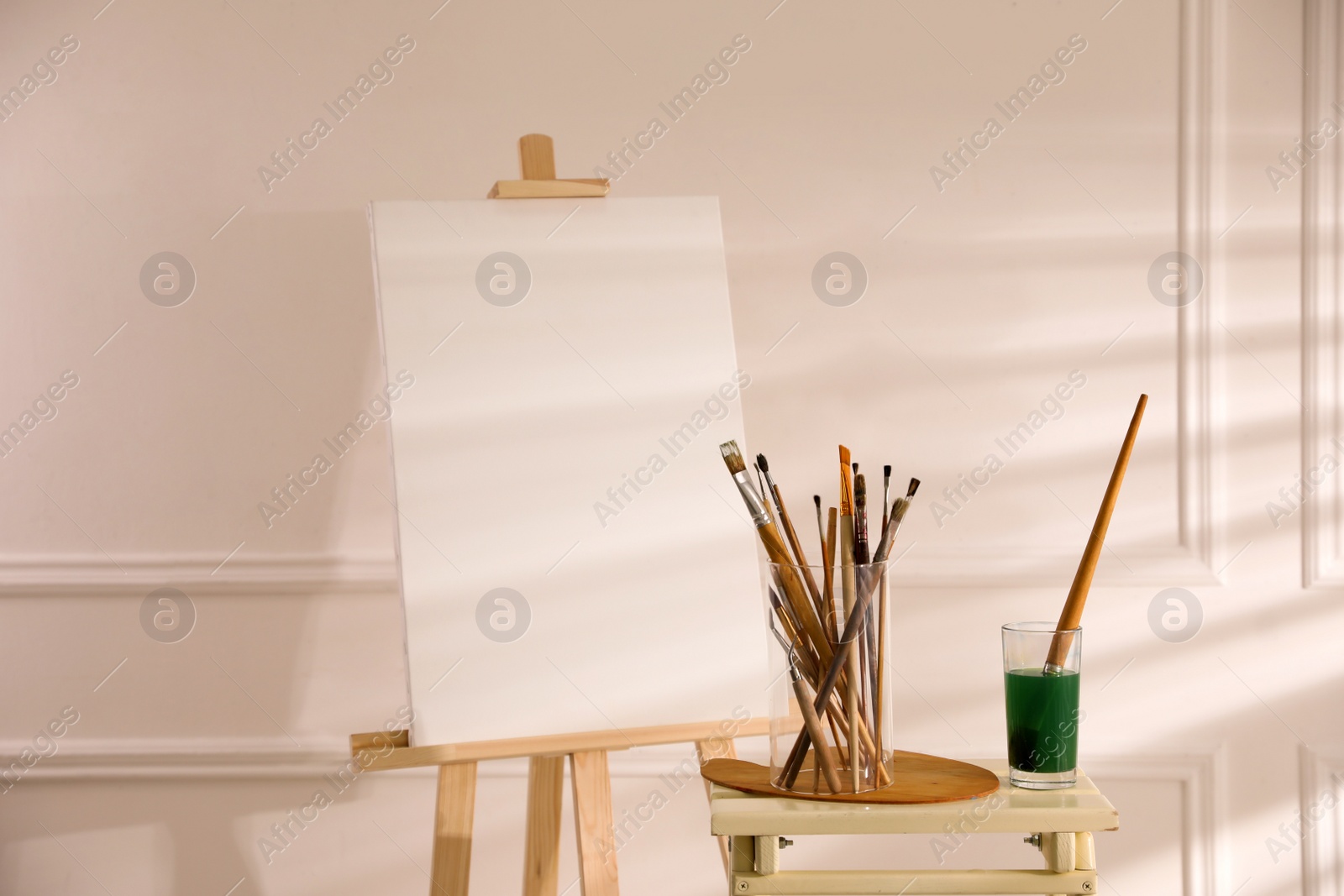 Photo of Wooden easel with empty canvas and brushes in art studio