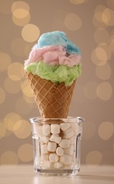 Photo of Sweet cotton candy in waffle cone on table against blurred lights, closeup