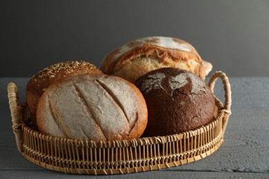 Wicker basket with different types of fresh bread on grey wooden table