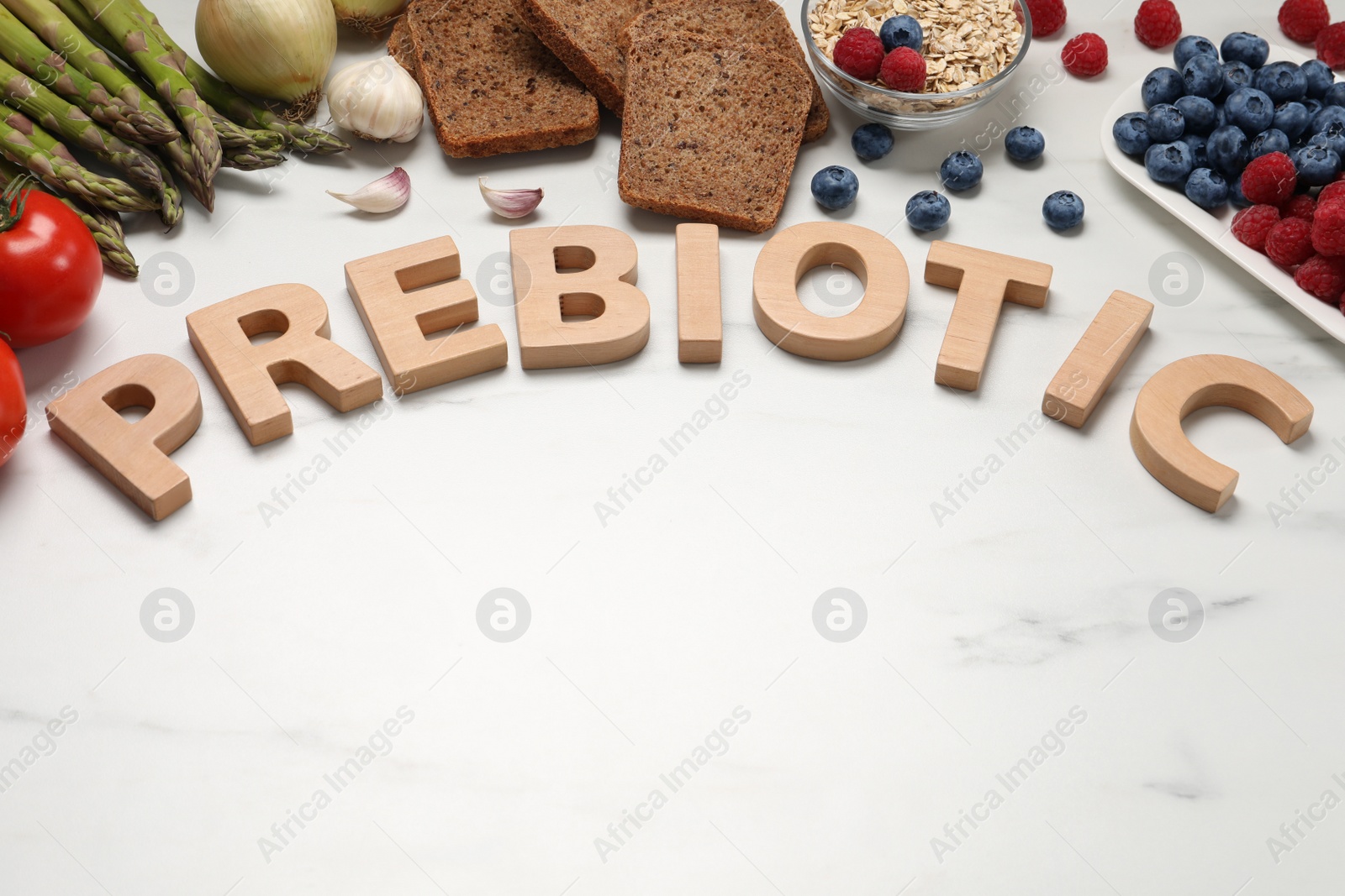Photo of Composition with word Prebiotic made of wooden letters and food on white marble table. Space for text