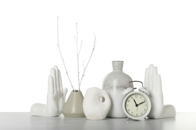 Different stylish vases, alarm clock and other decor elements on table against white background