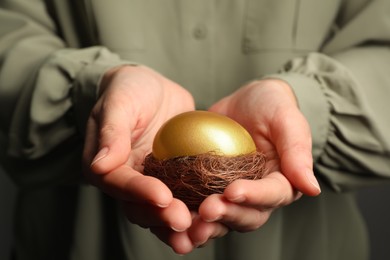 Photo of Woman holding nest with shiny golden egg, closeup