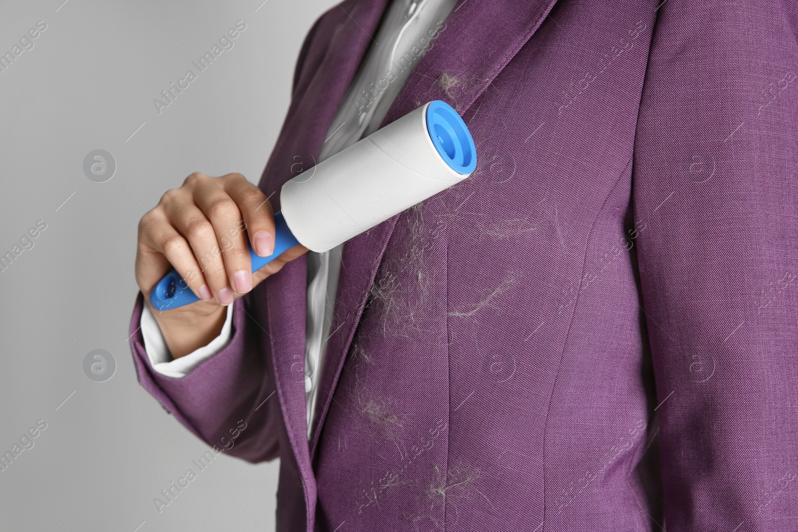 Photo of Woman removing hair from purple jacket with lint roller on light background, closeup