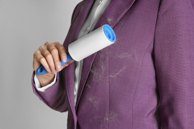 Woman removing hair from purple jacket with lint roller on light background, closeup