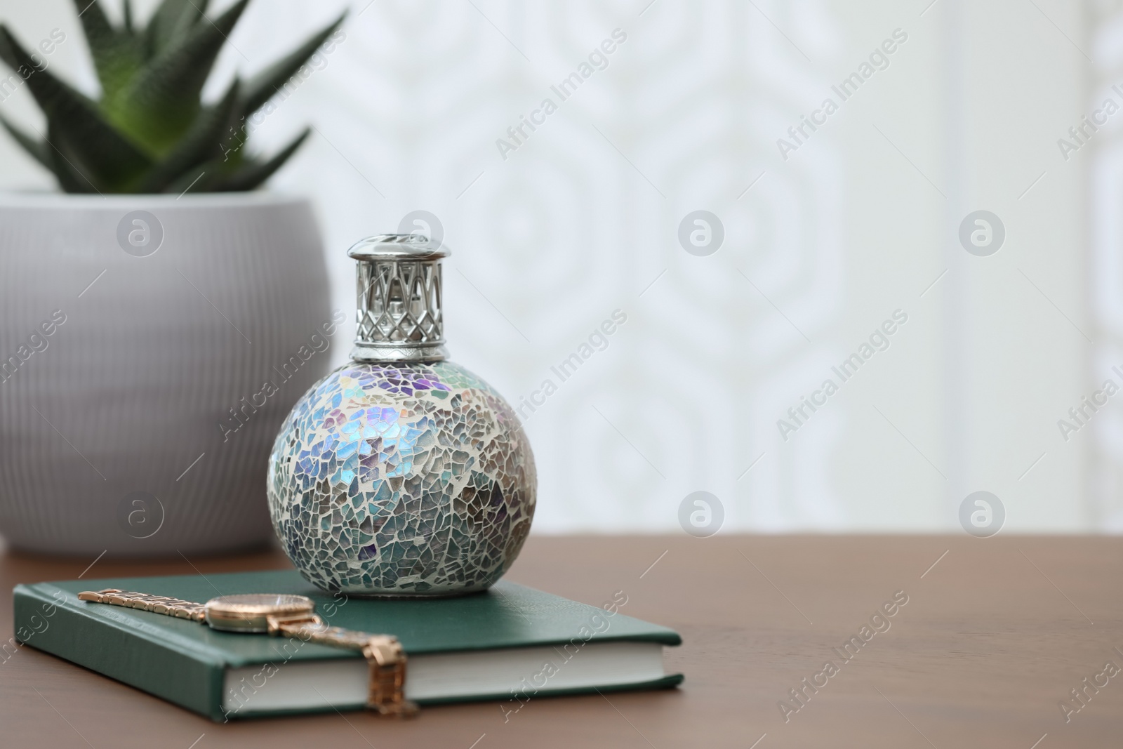 Photo of Burning catalytic purifying lamp, book and watch on wooden table, space for text