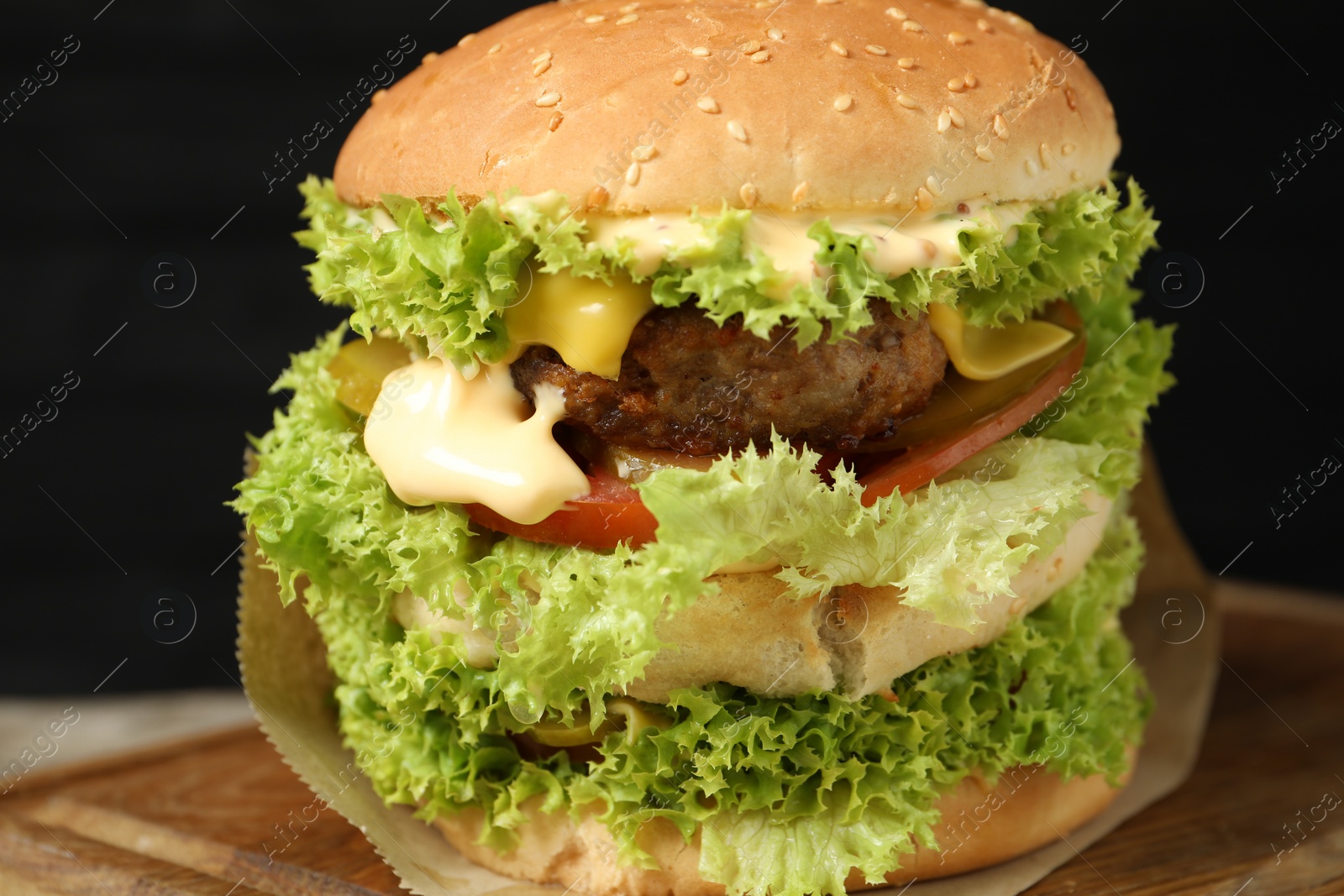 Burger with delicious patty on wooden table against dark background, closeup Photo of Burger with delicious patty on wooden table against dark background, closeup