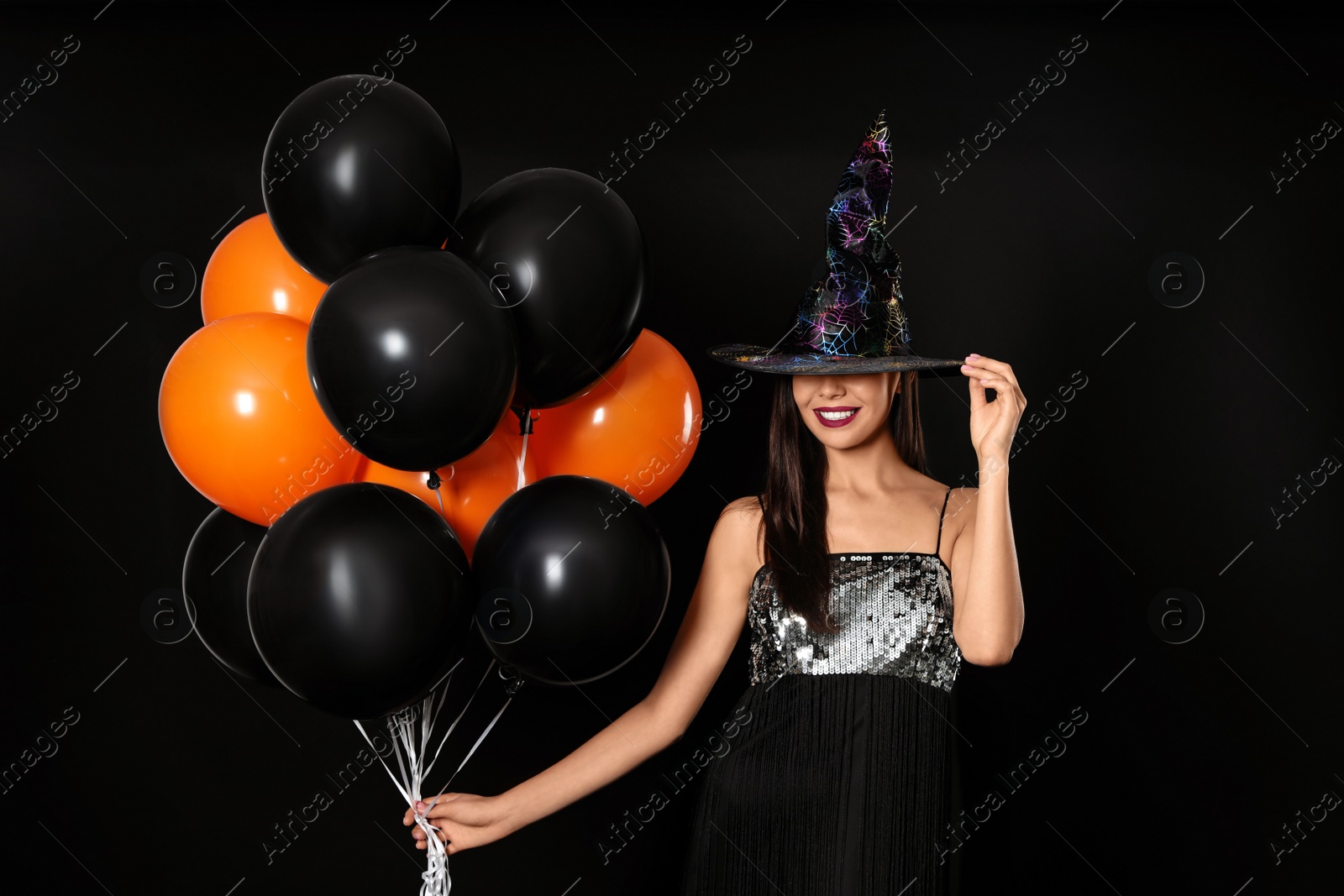 Photo of Beautiful woman wearing witch costume with balloons for Halloween party on black background