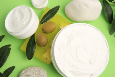 Photo of Different cosmetic products with olives and stones on light green background, flat lay