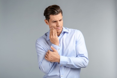 Young man suffering from toothache on grey background