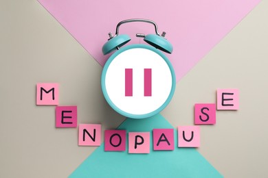 Menopause word of sticky notes with letters and alarm clock with pause symbol on color background, top view