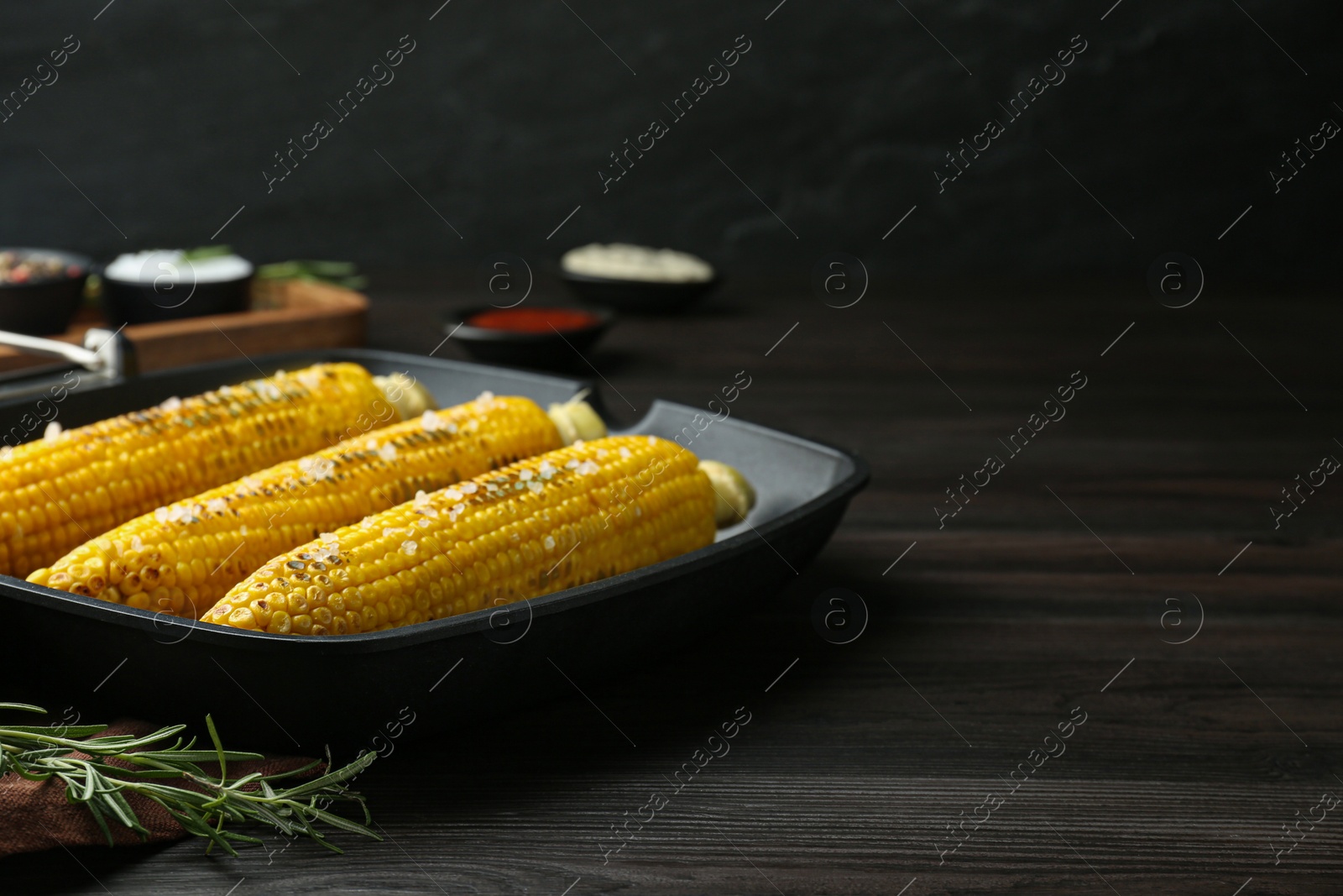 Photo of Grill pan with tasty frying corn on dark grey wooden table. Space for text