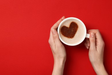 Photo of Woman holding cup of aromatic coffee with heart shaped decoration on red background, top view and space for text
