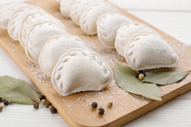 Photo of Raw dumplings (varenyky), peppercorns and bay leaves on white wooden table, closeup