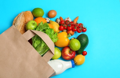 Photo of Paper bag with different groceries on light blue background, flat lay