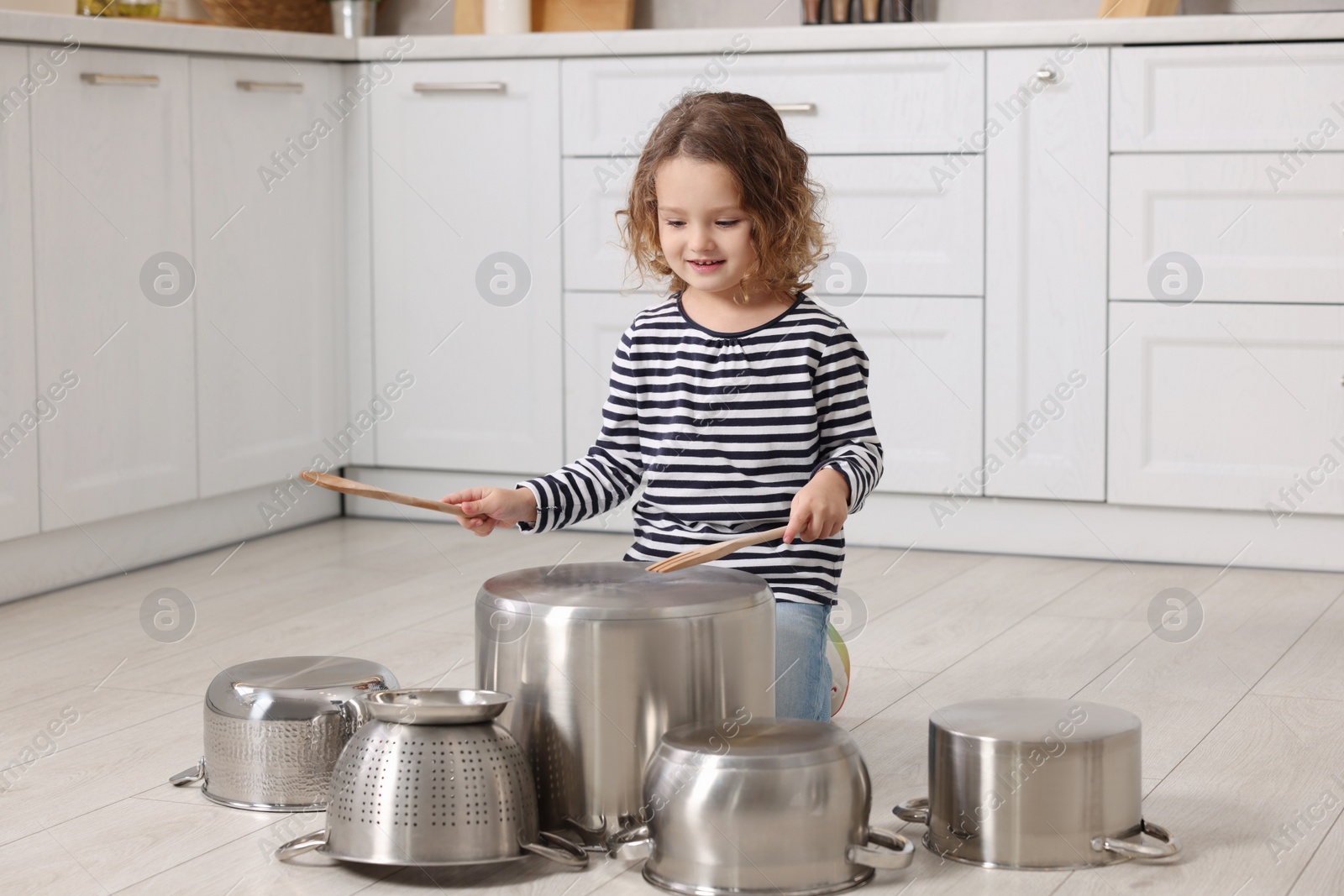 Photo of Little girl pretending to play drums on pots in kitchen