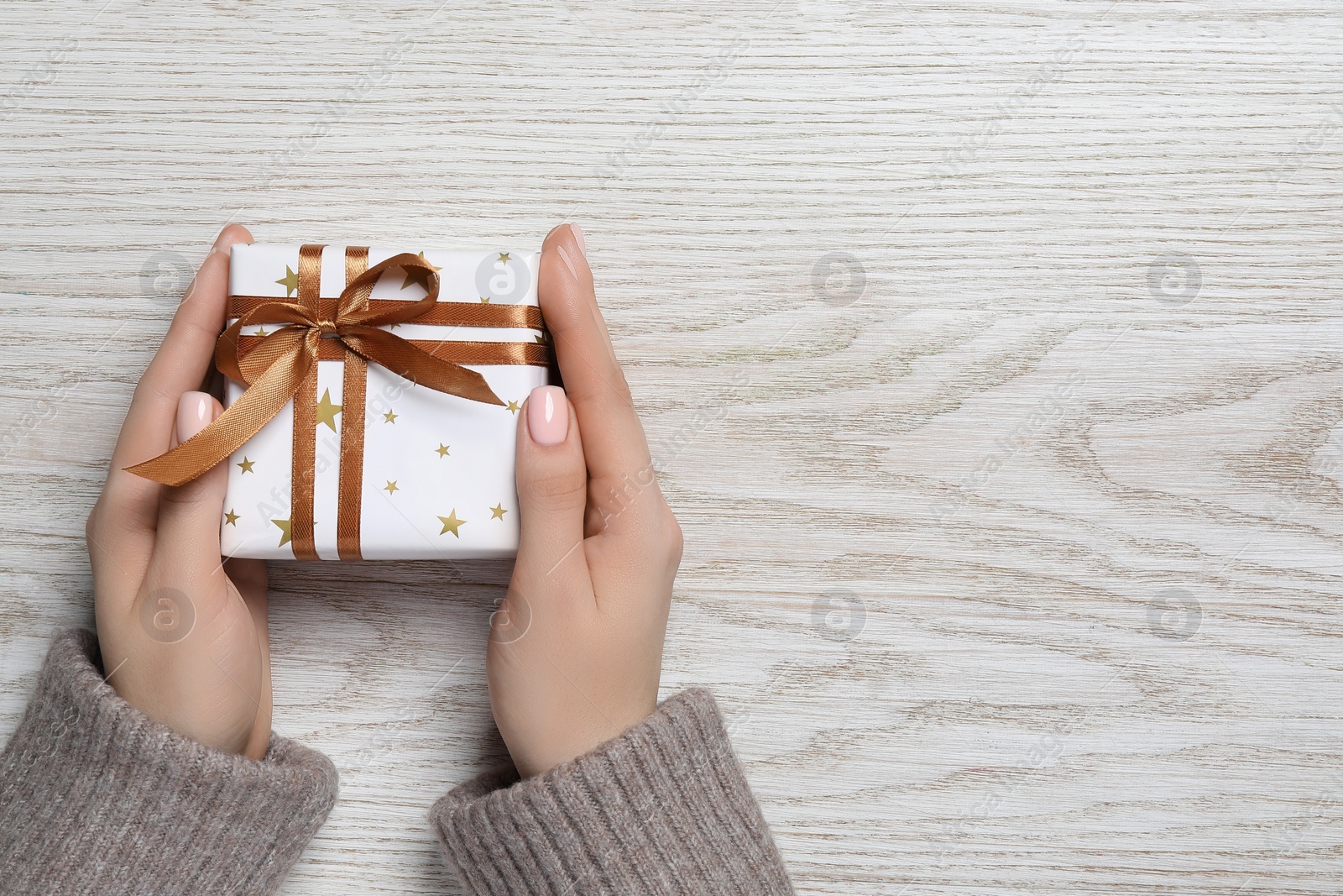 Photo of Christmas present. Woman holding gift box on white wooden background, top view. Space for text