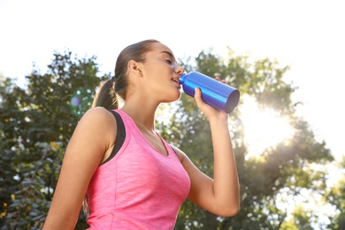 Photo of Young sporty woman drinking from water bottle in park on sunny day