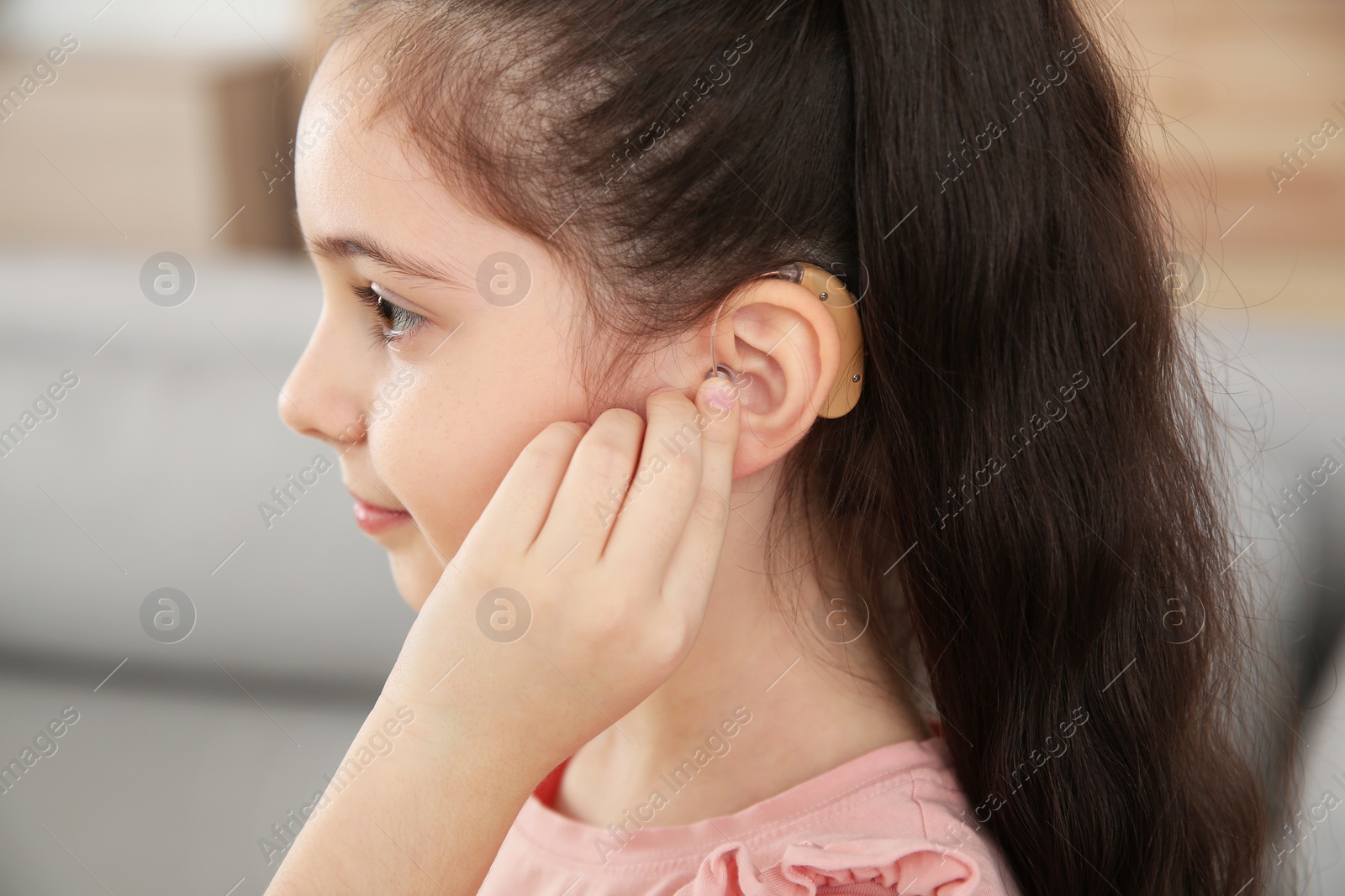 Photo of Little girl adjusting hearing aid at home