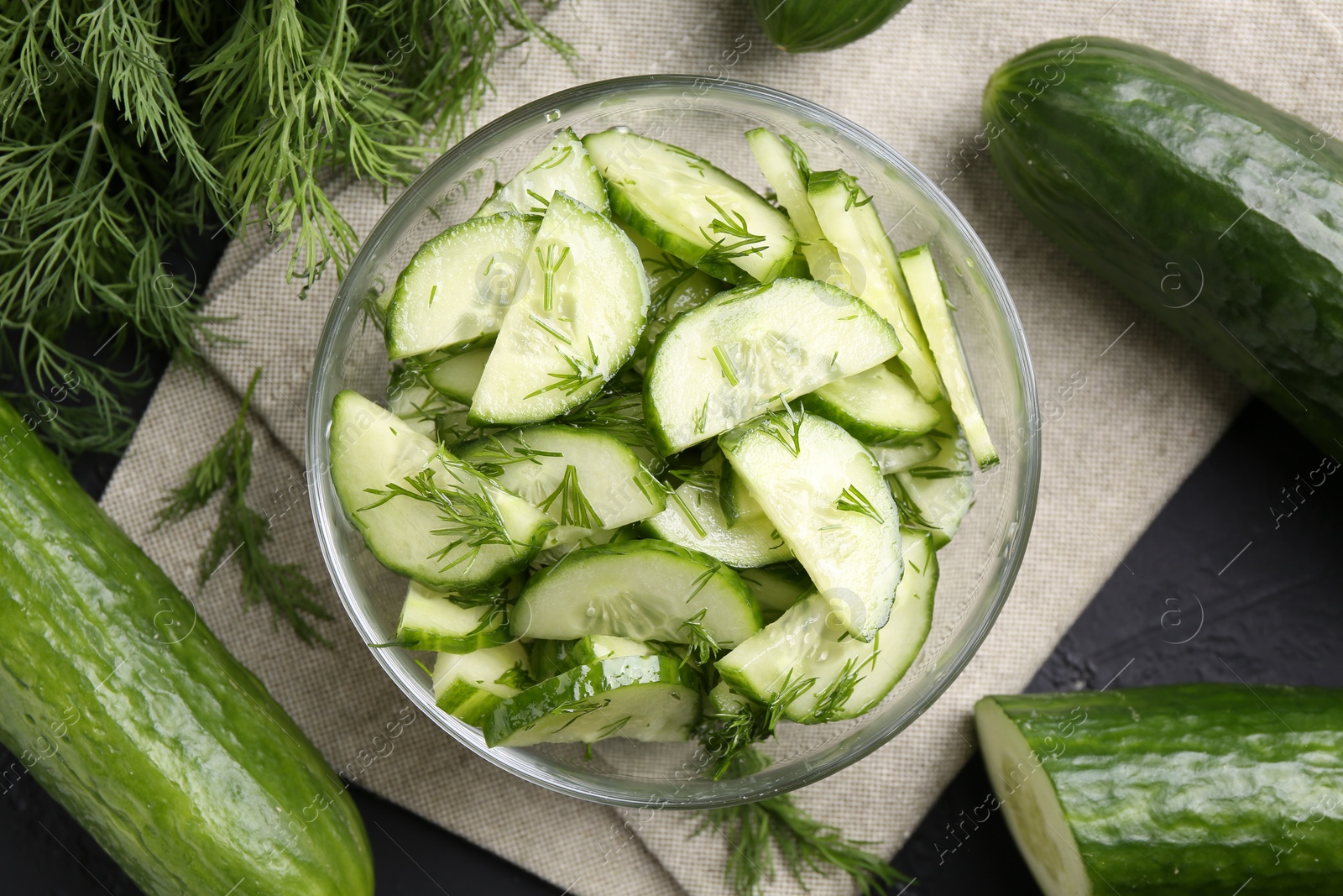 Photo of Cut cucumber with dill in glass bowl and fresh vegetables on table, flat lay