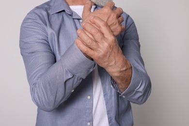 Senior man suffering from pain in hands on light grey background, closeup. Arthritis symptoms