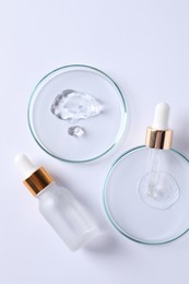 Photo of Petri dishes with samples of cosmetic serums, pipette and bottle on white background, flat lay