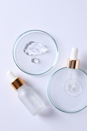 Petri dishes with samples of cosmetic serums, pipette and bottle on white background, flat lay