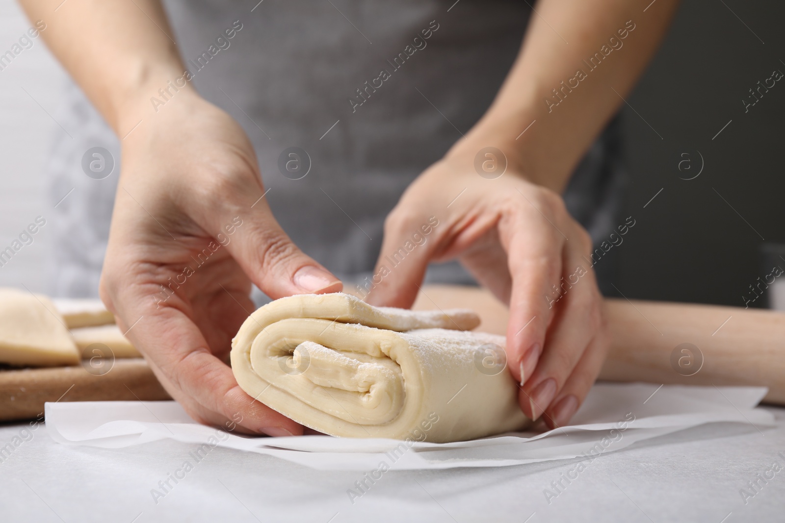 Photo of Woman with raw puff pastry dough at white table, closeup