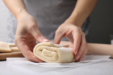 Woman with raw puff pastry dough at white table, closeup