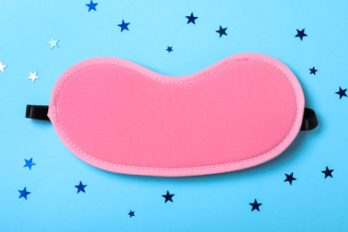 Photo of Pink sleeping mask and glitter on light blue background, flat lay. Bedtime accessory