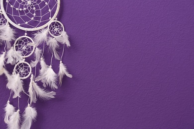 Beautiful handmade dream catcher on purple wall. Space for text