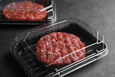 Photo of Plastic containers with raw meat cutlets for burger on grey table