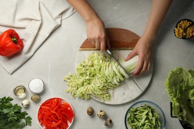 Photo of Woman cutting fresh Chinese cabbage at light grey table, top view