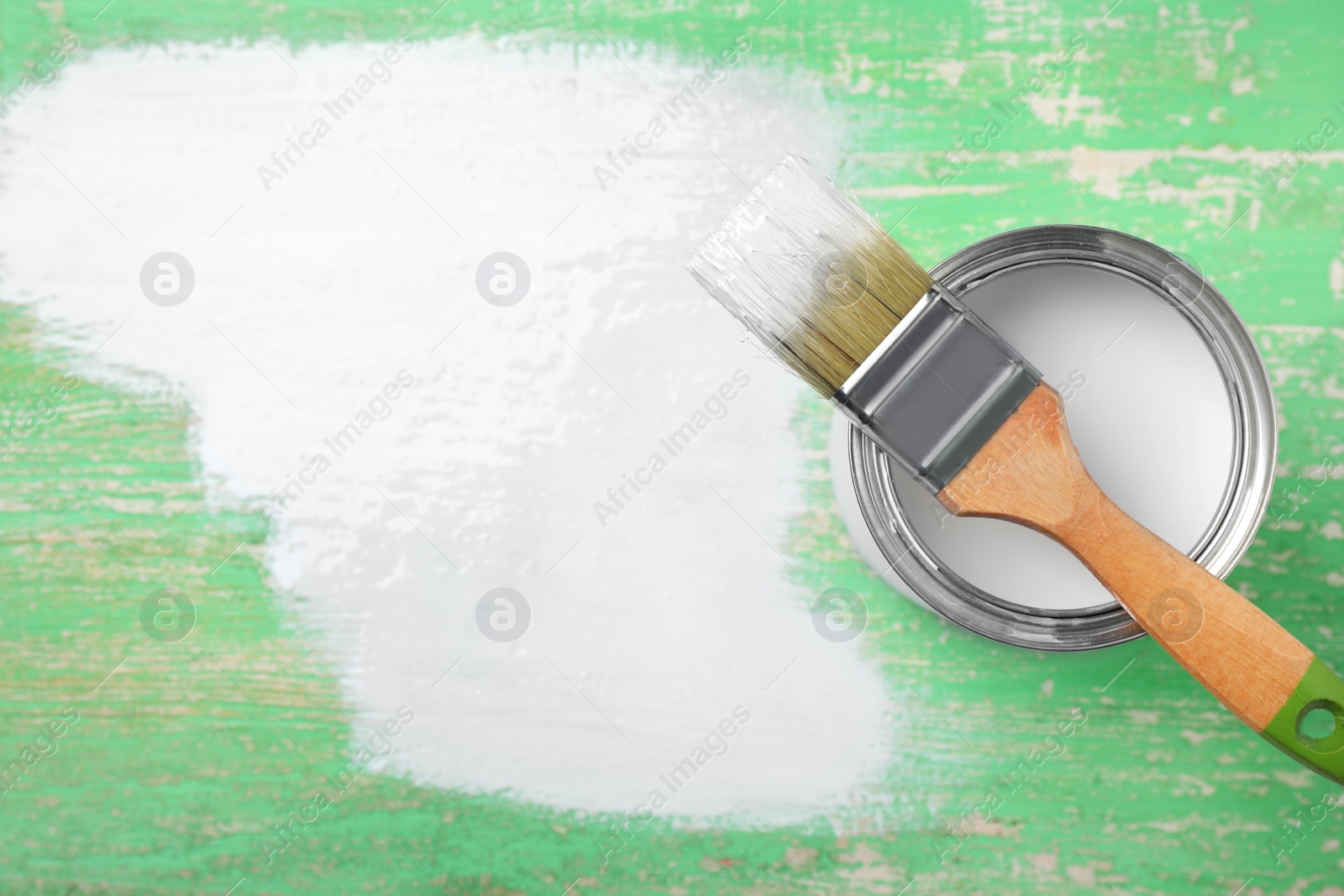 Photo of Can of white paint and brush on green wooden background, top view. Space for text