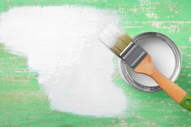 Can of white paint and brush on green wooden background, top view. Space for text