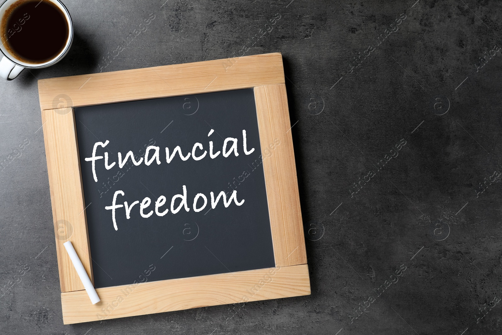Image of Small chalkboard with text Financial Freedom and cup of coffee on dark textured table, flat lay