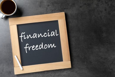 Small chalkboard with text Financial Freedom and cup of coffee on dark textured table, flat lay